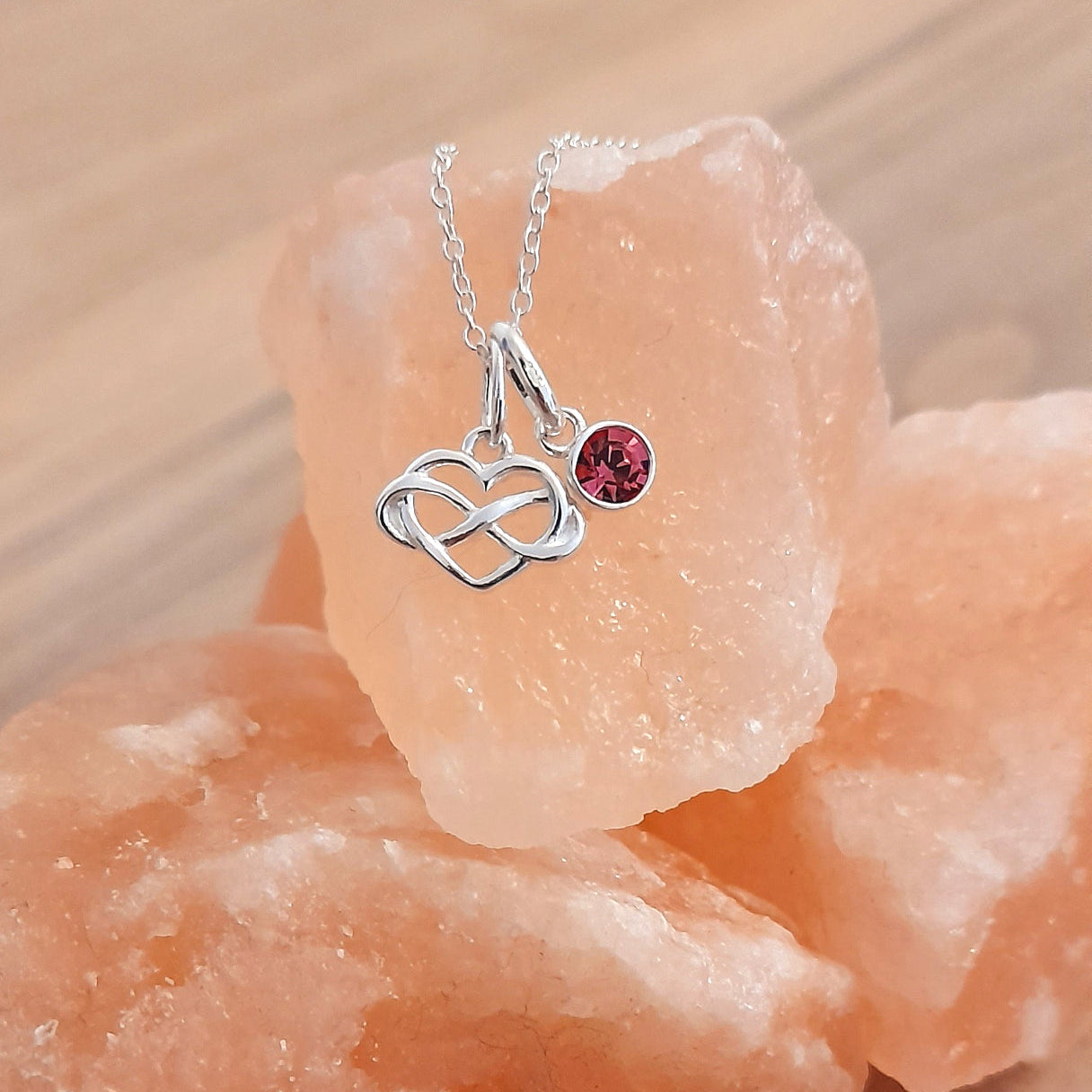 Silver necklace with a heart and infinity symbol pendant on a pink crystal background