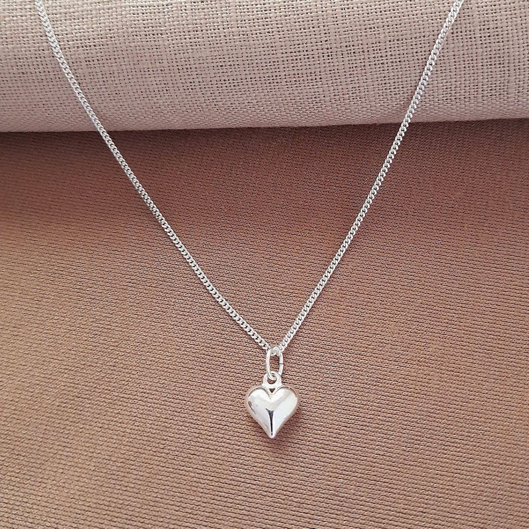 Silver heart-shaped pendant necklace on a beige fabric background