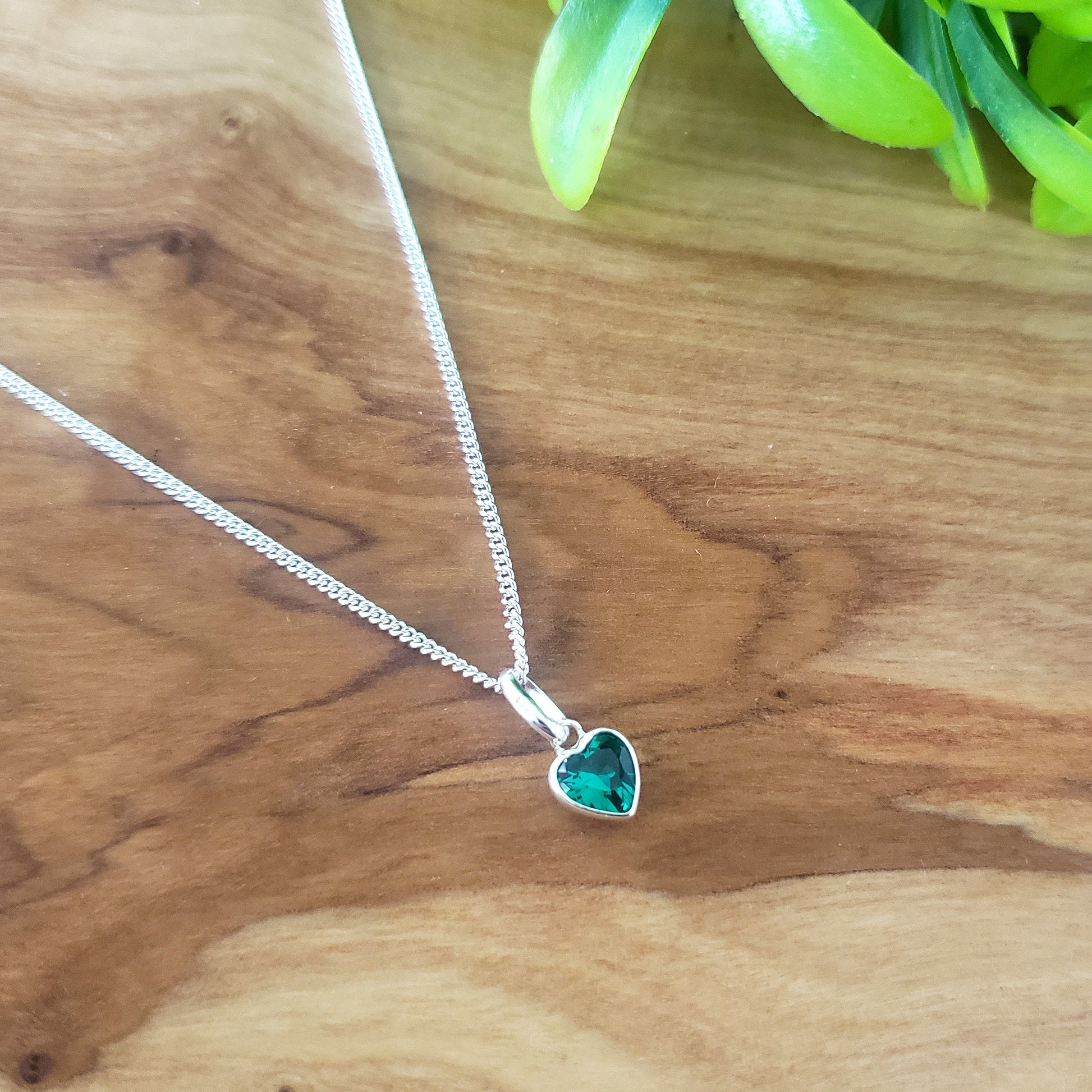 Necklace with a heart-shaped green gemstone pendant on a wooden surface.