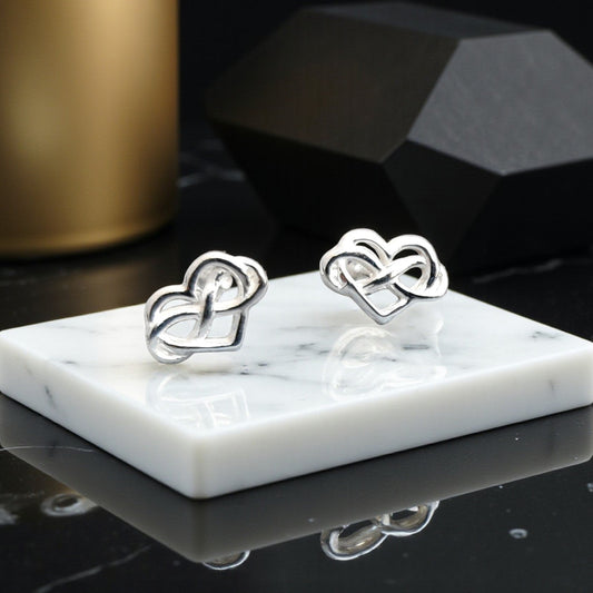Silver heart-shaped earrings on a marble stand with a dark background