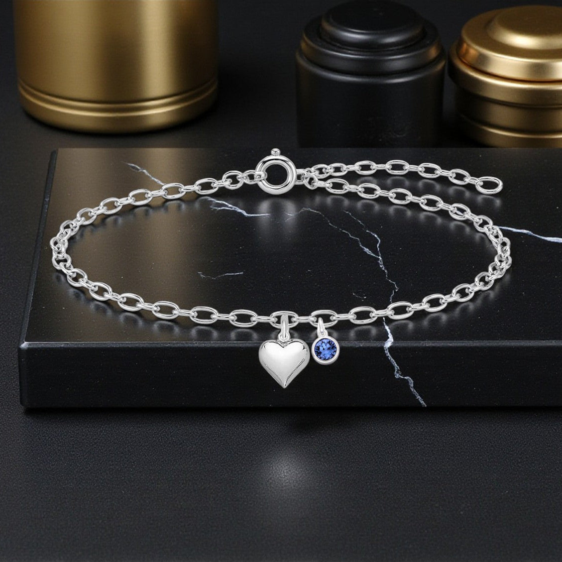 Silver bracelet with heart and blue gemstone charm on a black marble surface