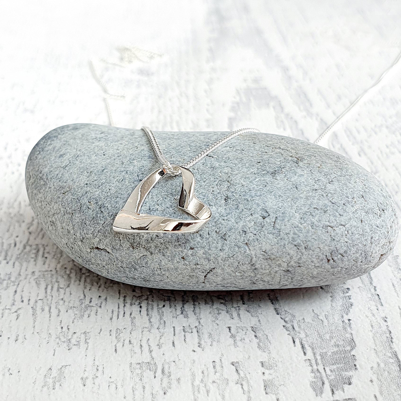 Silver necklace with a heart pendant on a gray stone surface